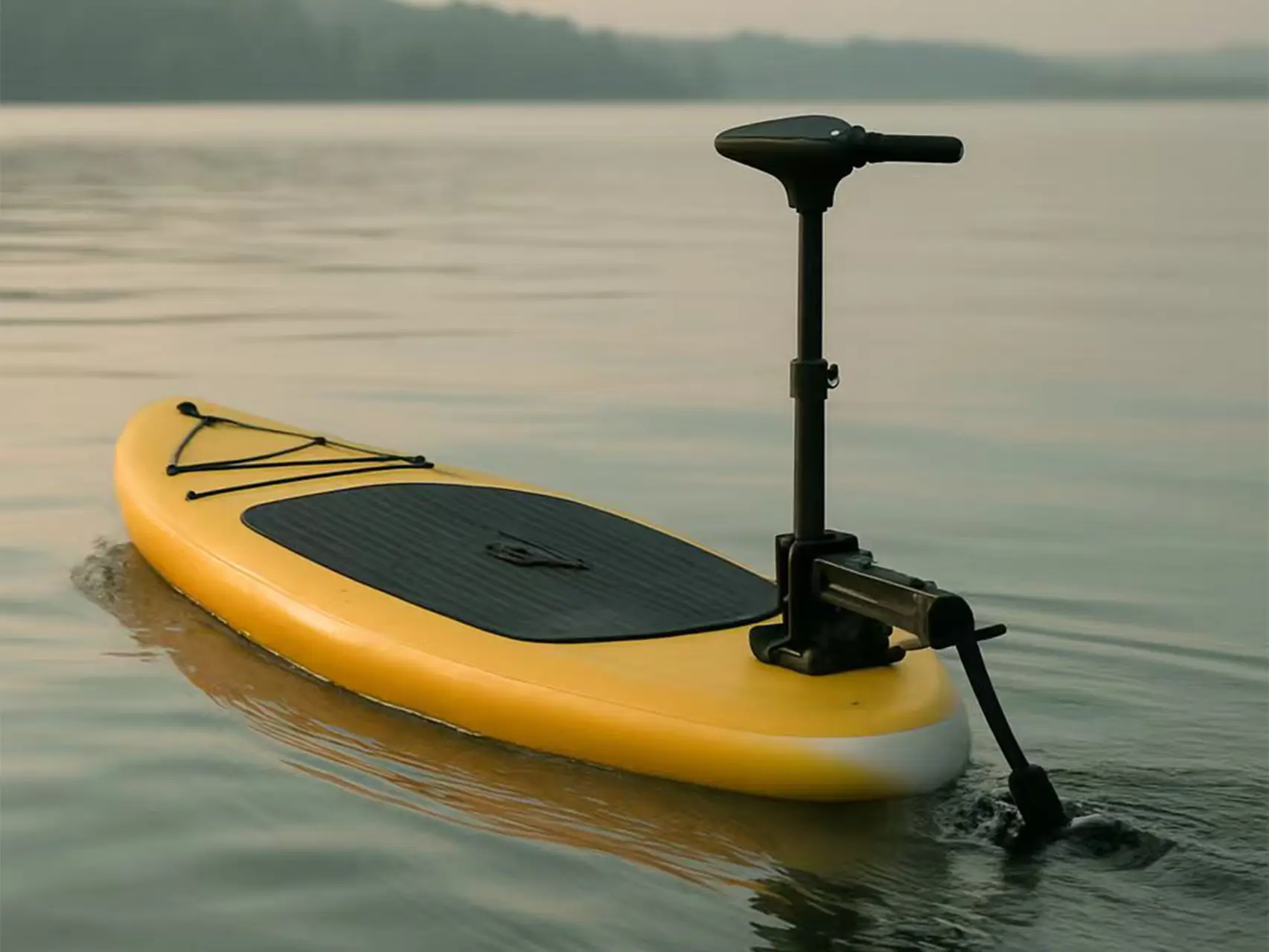 A yellow inflatable stand-up paddleboard with a black electric trolling motor mounted on the stern, gliding across a calm lake during sunset.