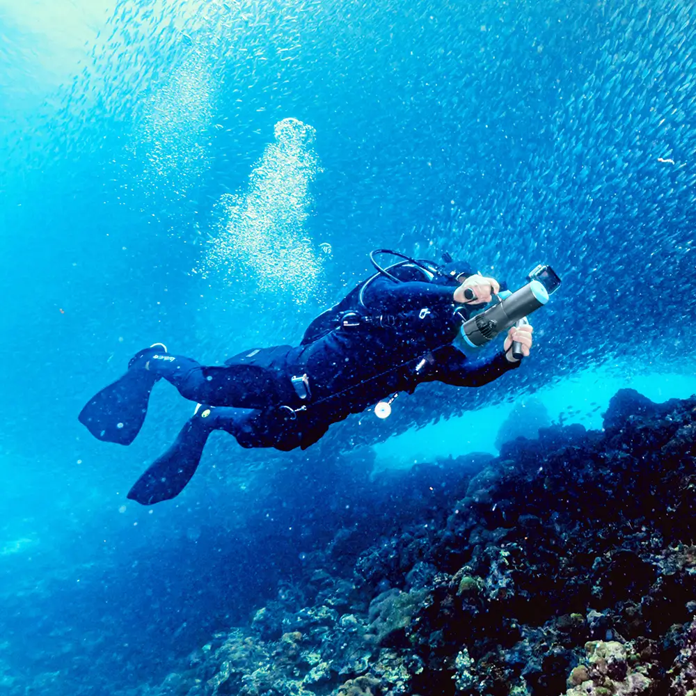 Scuba diver using TEDGIX K5 underwater scooter to swim effortlessly through a massive school of fish in the deep ocean.